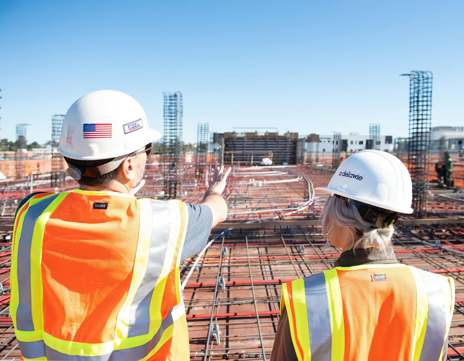 Two contractors in hard hats reviewing a rebar deck on an active construction site